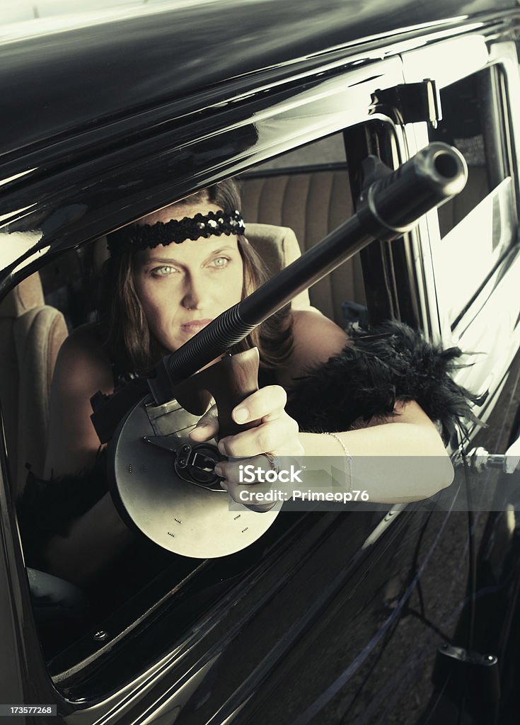 Dangerous Woman 1930s styl image with a woman holding a tommy gun.  Lighting is dramatic as if she is being spotlighted. Focus is on the drum of the tommy gun 1930-1939 Stock Photo