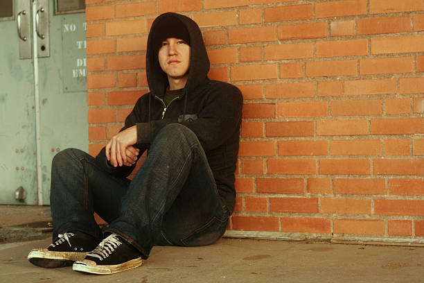 Punk and a hoodie with dirty shoes sitting by brick wall stock photo