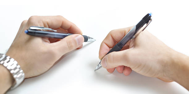 Two ambidextrious hands writing simultaneously. A left and right hand using matching blue pens to write simultaneously. ambidextrous stock pictures, royalty-free photos & images