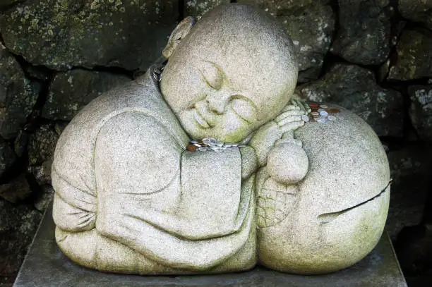 "A stone sculpture of a young sleeping Buddhist monk, resting on a wooden drum with stick in hand. People place money on the statue to bring themselves good luck and prosperity, and to donate to the Buddhists in the area. This is one of many public statues display around Koya-san, a quiet mountain retreat and the headquarters of the Shingon sect of Japanese Buddhism."