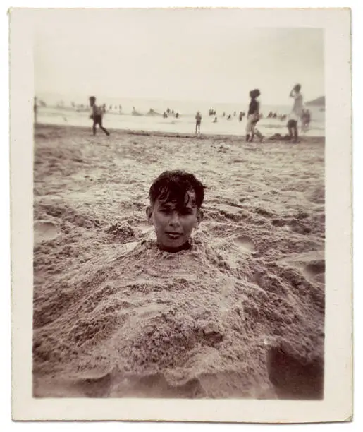 Photo of Vintage photo of boy buried in sand at the beach