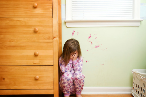 Five-year-old girl ashamed and worried because she painted on the wall.