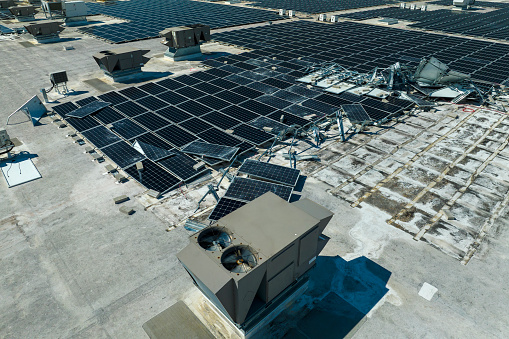 Broken down photovoltaic solar panels destroyed by hurricane Ian winds mounted on industrial building roof for producing green ecological electricity. Consequences of natural disaster.