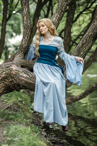 A young beautiful girl in a summer park. A beautiful medieval elf princess in a blue dress in the forest