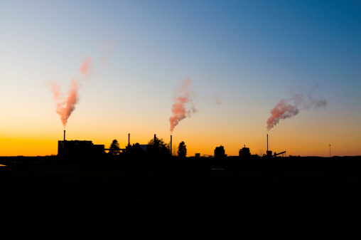 Three smoking chimneys against sunset.