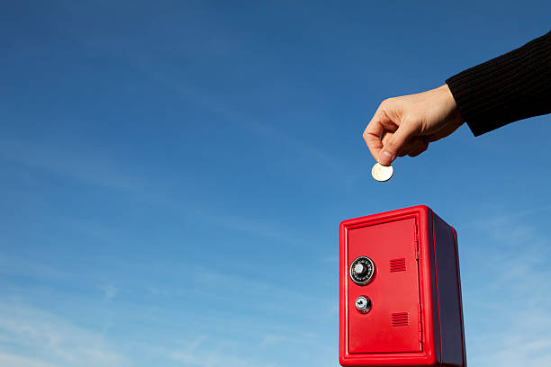 Hand Putting Coin into Red Safe Money Box stock photo