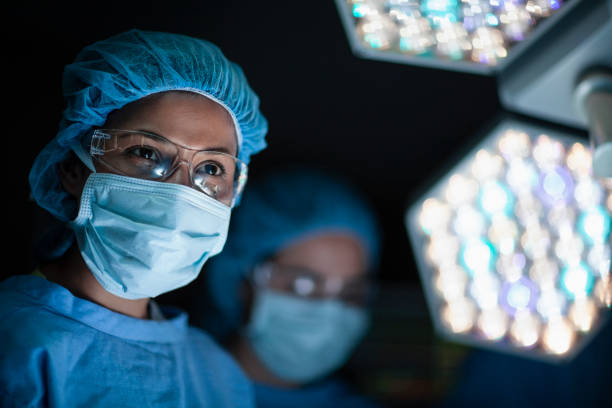 médico hispano sonríe a la enfermera en la sala de operaciones de cirugía con colegas y luces en el hospital - hair net nurse scrubs asian ethnicity fotografías e imágenes de stock