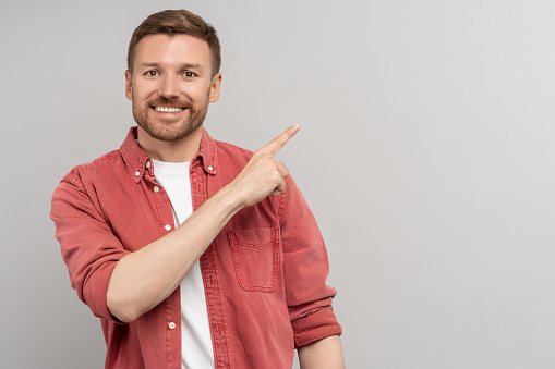 Cheerful middle aged man points index finger by side on empty space on background. Banner for advertising, marketing, sales, good offer, discount. Fascinating male promoter smiling looking at camera.