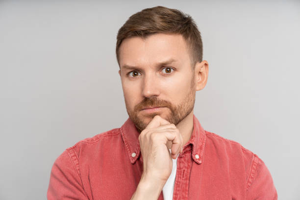 istock Puzzled thoughtful pensive man looking at camera touching chin feeling doubts isolated background. 1735864842