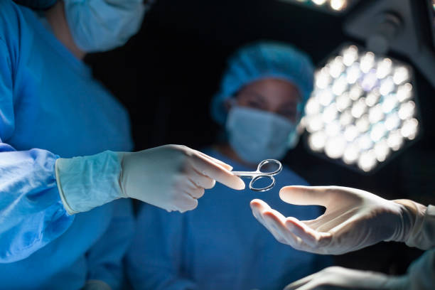 médico profissional enfermeiro passando ferramenta cirúrgica de mão em mão para colega em sala de cirurgia no hospital - nurse reaching women doctor - fotografias e filmes do acervo