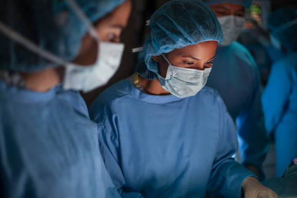 Hispanic medical professional doctor nurse looking down serious in concentration towards patient in surgery operation room in hospital with colleagues stock photo