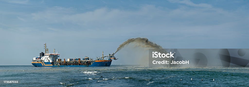 Making New Land Ship spouting sand in front of the coast to gain new land from the sea. Giant panoramic stitch of 12 shots. Beach Stock Photo