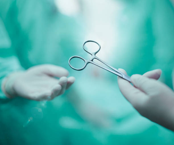 mão de enfermeira passando ferramenta médica para médico palma da mão usando roupa de trabalho protetora em sala de cirurgia médica no hospital com paciente incidental pessoas fundo com luz - nurse reaching women doctor - fotografias e filmes do acervo