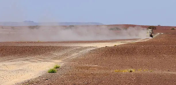 A Landrover driving through an African desert with a long dust trail behind it.