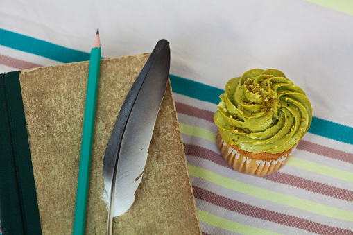 Still life with an old book, a cupcake, a feather and a pencil