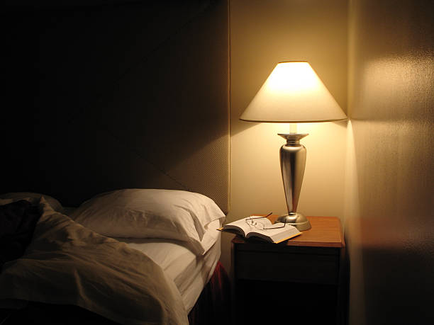 Bed Turned Down in Hotel Room Night scene in hotel room, nightstand with lamp, bed turned down, opened book and reading glasses. 1st in series. Great wall reflection and texture. night table stock pictures, royalty-free photos & images