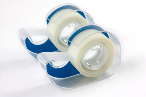 Two plastic disposable tape dispensers isolated on a white background. The adhesive tape is clear and  has a blue backing on the roll. The selective focus is on the closer roll and falls off by the back one. - A great isolated object shot isolated on a white background.