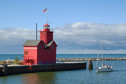 Yacht passing the Holland Harbor Light (1907), commonly known as Big Red; the iconic landmark is located at the entrance of a channel connecting Lake Michigan with Lake Macatawa, and which gives access to the city of Holland, Michigan