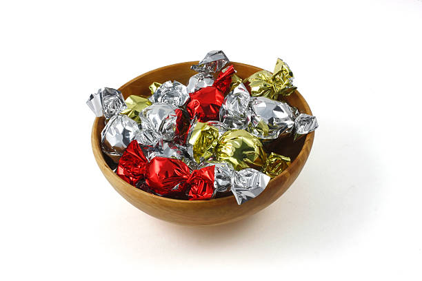 Candies in yellow and red wrappers standing in artificial snow. Christmas festive treats in golden foil. Copy space