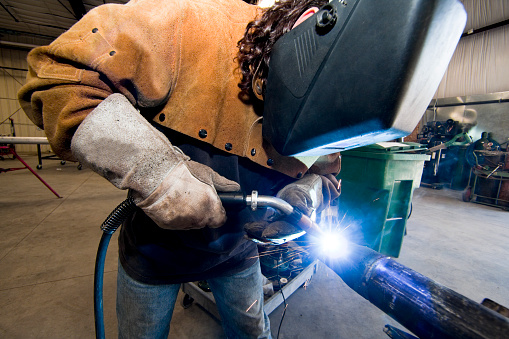 Worker with welder's mask welding pipe