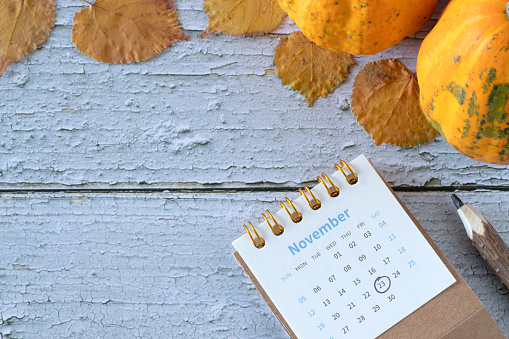 23 November date in calendar with autumn leaves and pumpkin on wooden background. Thanksgiving day concept. Top view, copy space.