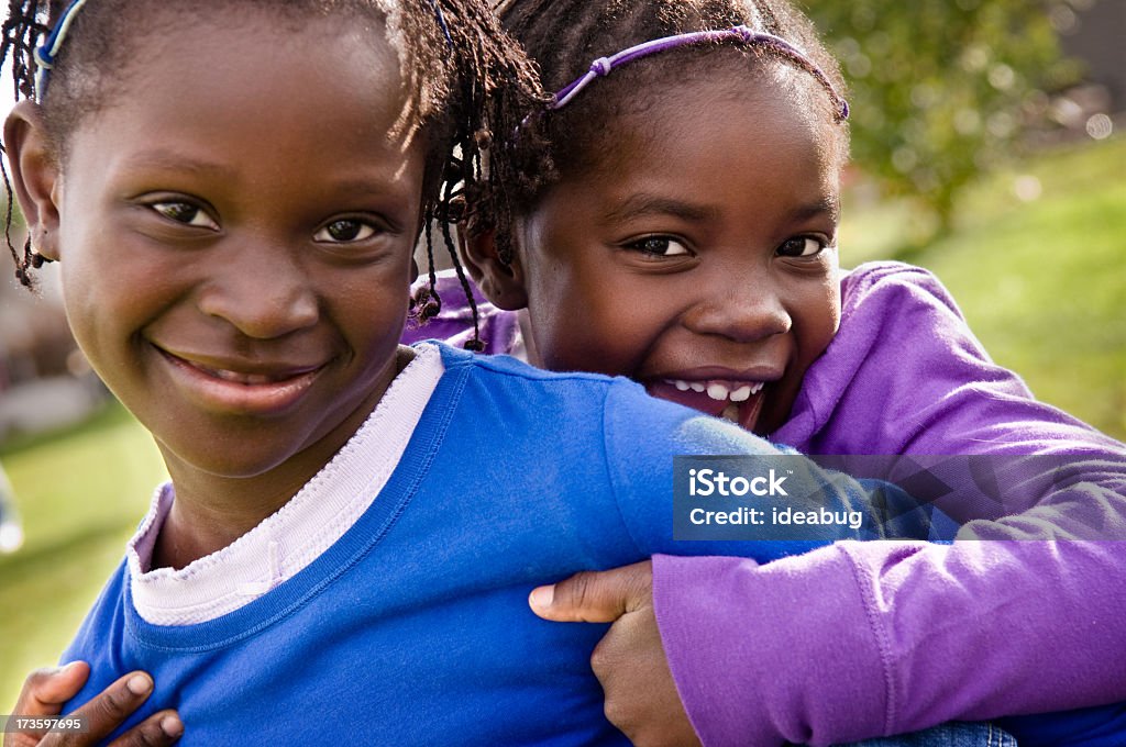 Due bambine felici sorridenti e abbracciare all'aperto - Foto stock royalty-free di Abbracciare una persona