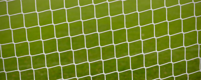 Close-up of the net of a soccer goal with the empty soccer field in blurred background.