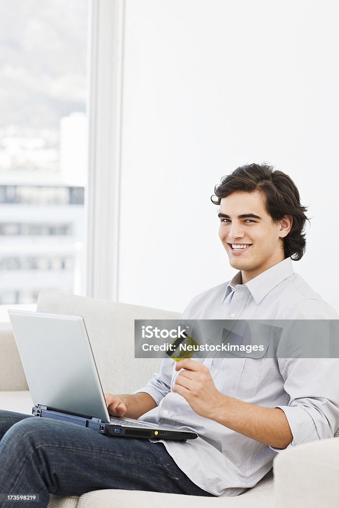 Felice uomo che tiene la carta di credito e utilizzando il computer portatile - Foto stock royalty-free di 20-24 anni