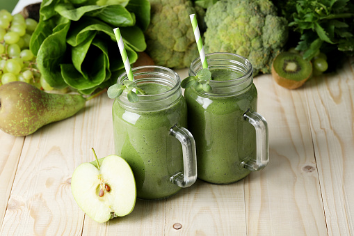 Mason jars of fresh green smoothie and ingredients on wooden table