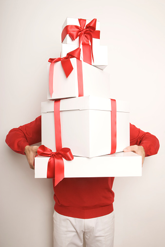 A pair of red-clad arms reaches around holding up a stack of red bow Christmas holiday presents piled high