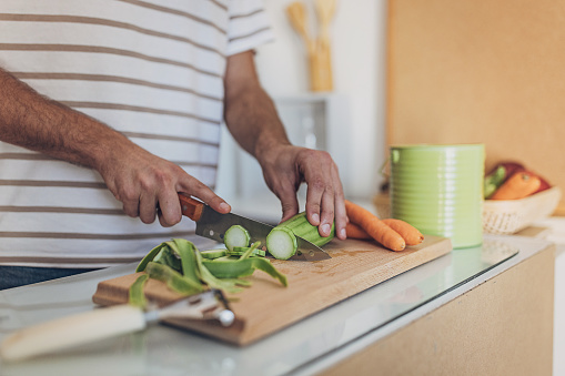 Man preparing a fresh, healthy meal in a modern domestic kitchen. He's smiling, focused, and chopping vegetables on a cutting board. It's a glimpse into his contented, enjoyable routine