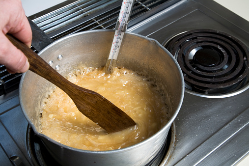 English toffee, a sugar and butter based confection, after it has caramelized, and just before it reaches the final temperature at which it becomes hard candy. Saucepan, candy thermometer, wooden spoon, chrome stovetop.