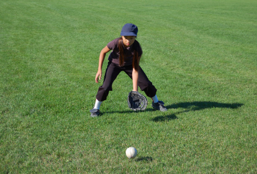 Young girl catches a softball in the outfield of a baseball diamond.