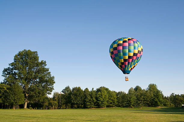 Large pink blue and yellow hot air balloon flying over grass stock photo