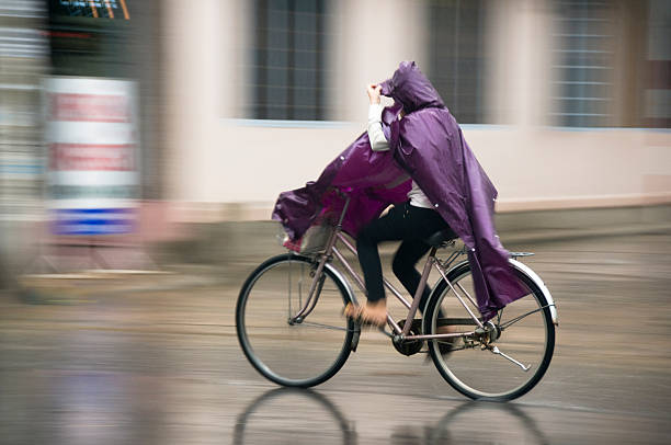 frau auf einem fahrrad im regen - drenched raincoat rain clothing stock-fotos und bilder
