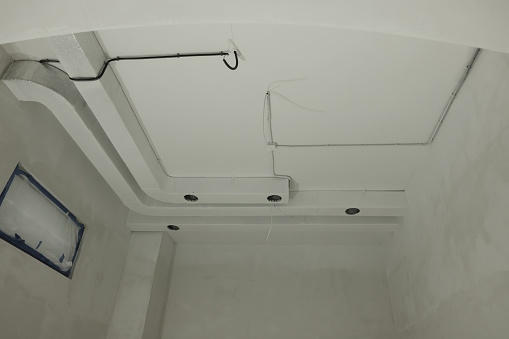 Ventilation system and wires on white ceiling indoors