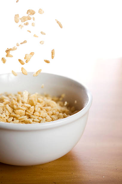 Rice Breakfast Cereal Pouring Into Bowl A bowl of baked grain cereal being poured, morning light pouring in from a nearby window. Vertical with copy space. rice cereal plant stock pictures, royalty-free photos & images