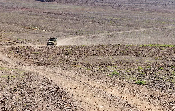 A Landrover driving through an African desert with a long dust trail behind it.