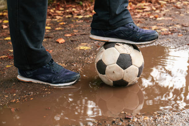 Man with soccer ball in muddy puddle outdoors, closeup