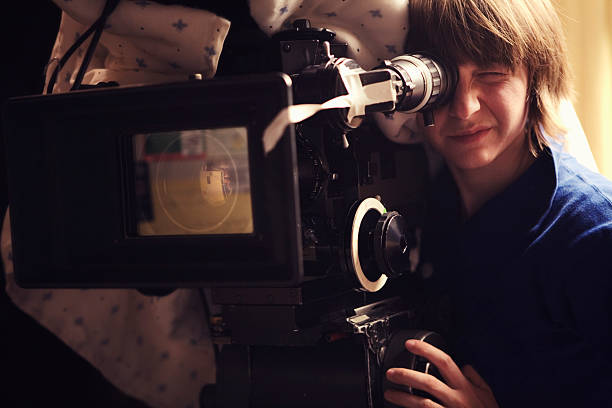 Filming "A young woman operating a 35mm film camera. There is a blanket thrown over the camera to dampen the sound of the film running through it so it doesn't interfere with the scene.Shot on a real set at high iso, some noise, view at 100%.More filmmaking images:" camera man stock pictures, royalty-free photos & images
