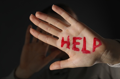 Woman with word Help written on hand against black background, closeup.