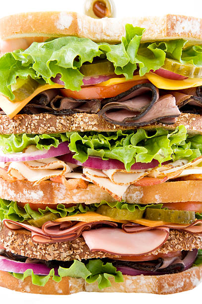 Dagwood Delight Full frame of the layers of a huge sandwich with various deli meats, pickles, onions,bacon, lettuce and cheese dagwood stock pictures, royalty-free photos & images