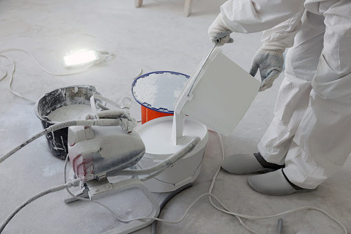 Decorator pouring paint in bucket on white floor, closeup