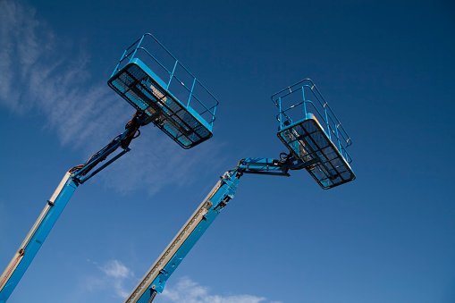 Two blue cherry picker lifts against a blue sky