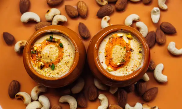 Kulfi ice cream in two clay pots on a solid orange background with cashews and almonds. Kulfi is a popular traditional Indian dessert made of milk with spices and nuts.