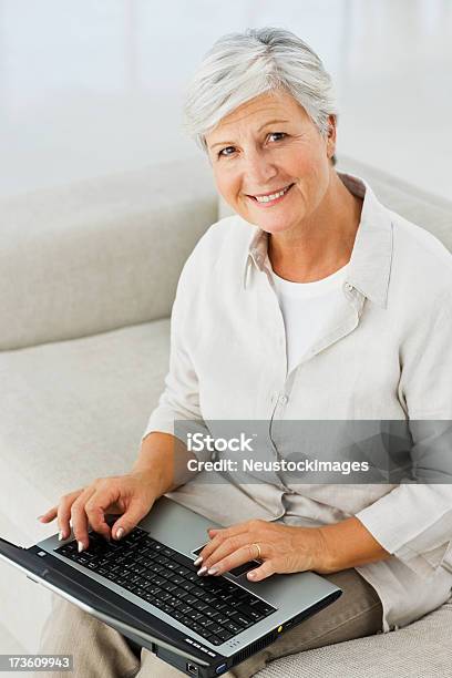 Senior Mujer Sentada En El Sofá Y Usando La Computadora Portátil Foto de stock y más banco de imágenes de 60-64 años