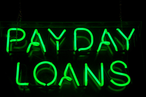 Payday Loans sign glows in green neon message on a black background