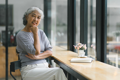 Beautiful asian senior woman with grey hair smiling while relaxing at cafe