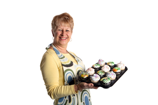 A woman holding a tray of a dozen cupcakes.