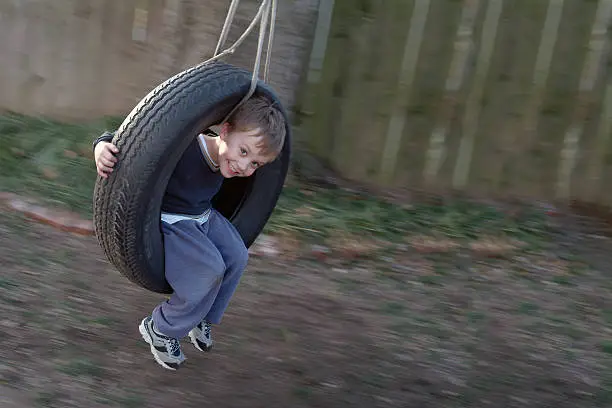 Horizontal image of young boy in motion on tire swing. Focus is on his face and the background has motion blur. Wonderful expression of excitement and innocence on the boy's face as he plays on an evening in the Spring.